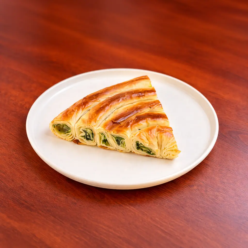 Crispy spinach börek triangle with flaky golden phyllo dough and fresh spinach filling served on a white plate at Cafe Galata Guelph