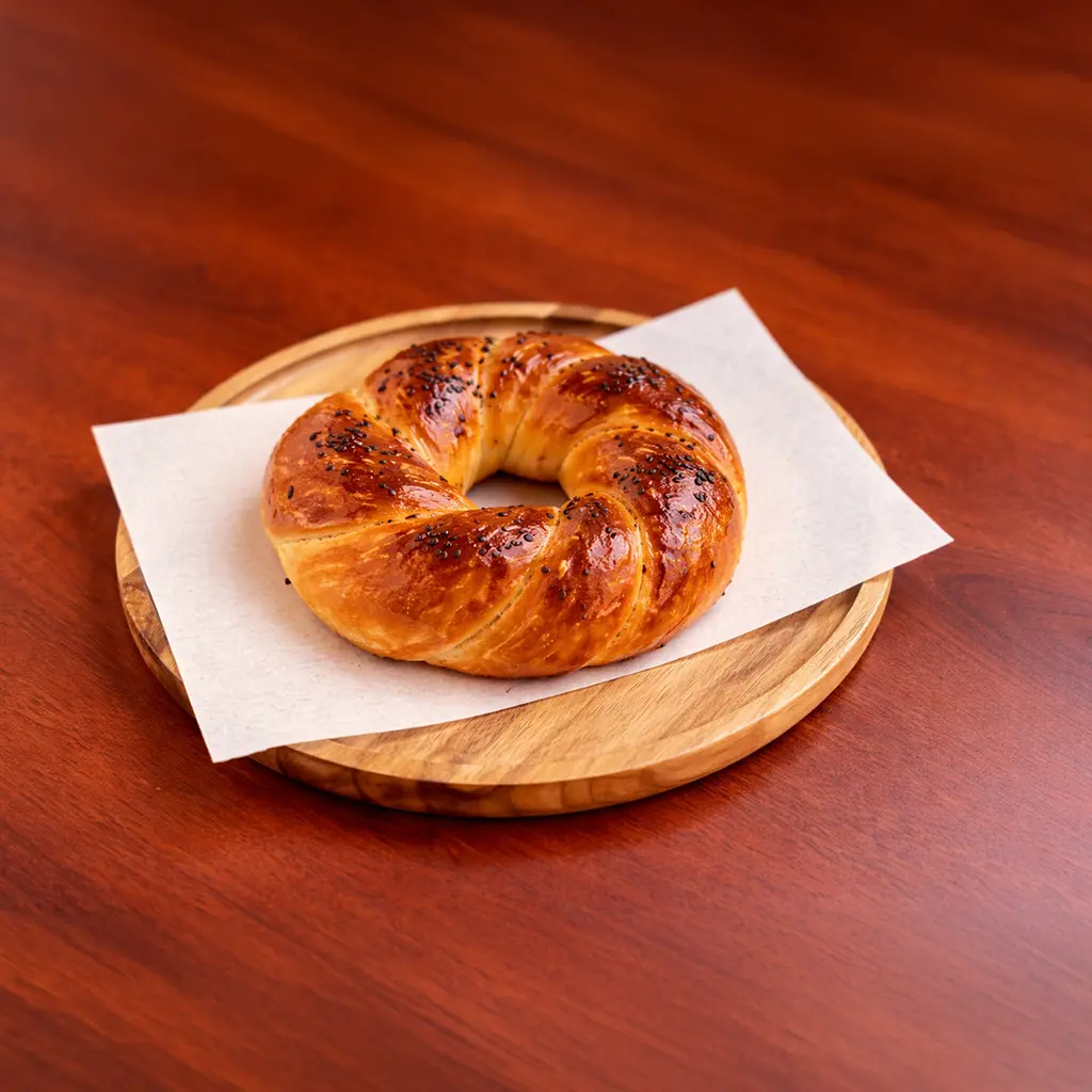 Freshly baked Turkish açma butter roll with black sesame seeds on a round wooden board at Cafe Galata in Guelph