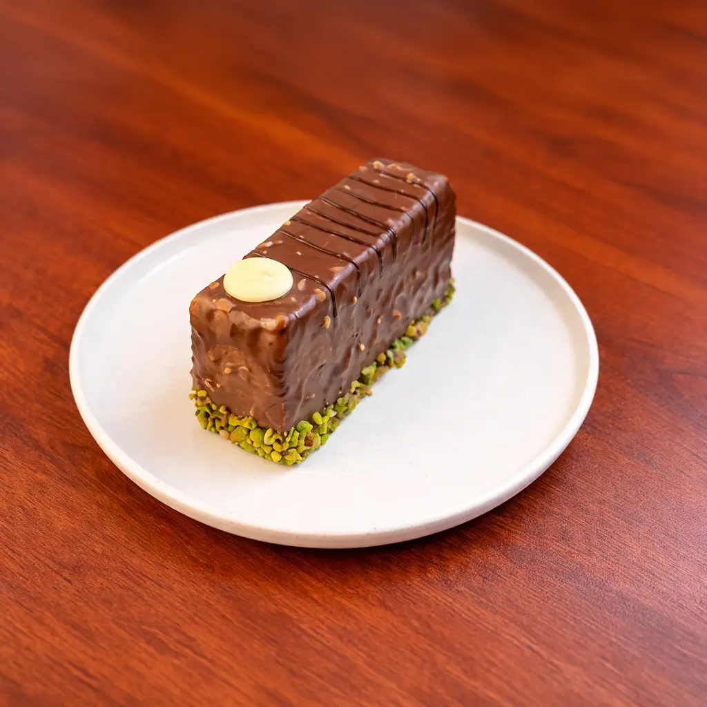 Hazelnut chocolate cake bar coated in milk chocolate and crushed hazelnuts with a pistachio crumb base and white chocolate disc garnish at Cafe Galata Guelph