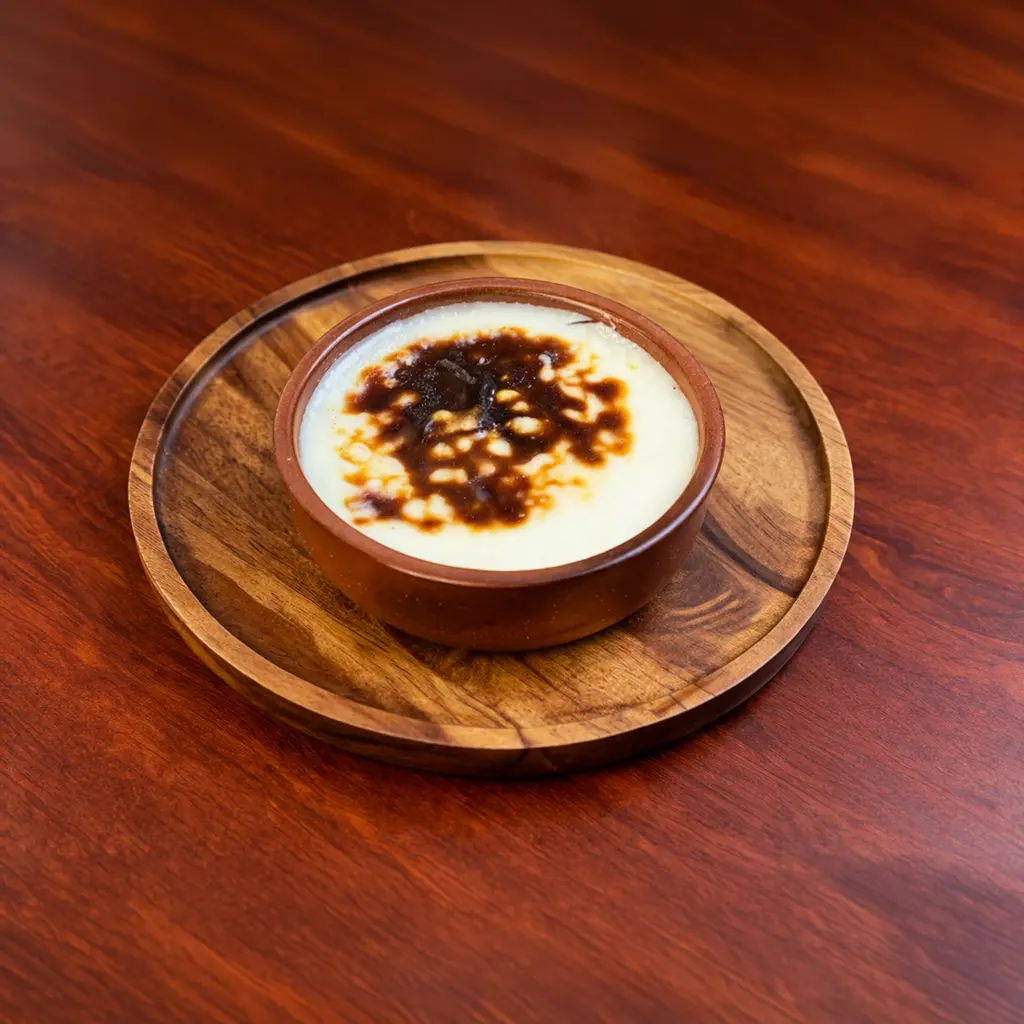 Oven baked Turkish rice pudding Sütlaç served in a clay bowl with a golden caramelized top on a wooden round tray at Cafe Galata Guelph