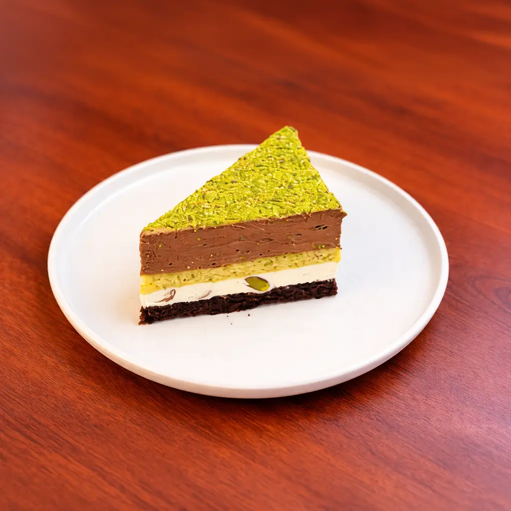 Pistachio line cake slice with dark chocolate brownie base, white cream, pistachio mousse and pistachio powder layers at Cafe Galata Guelph