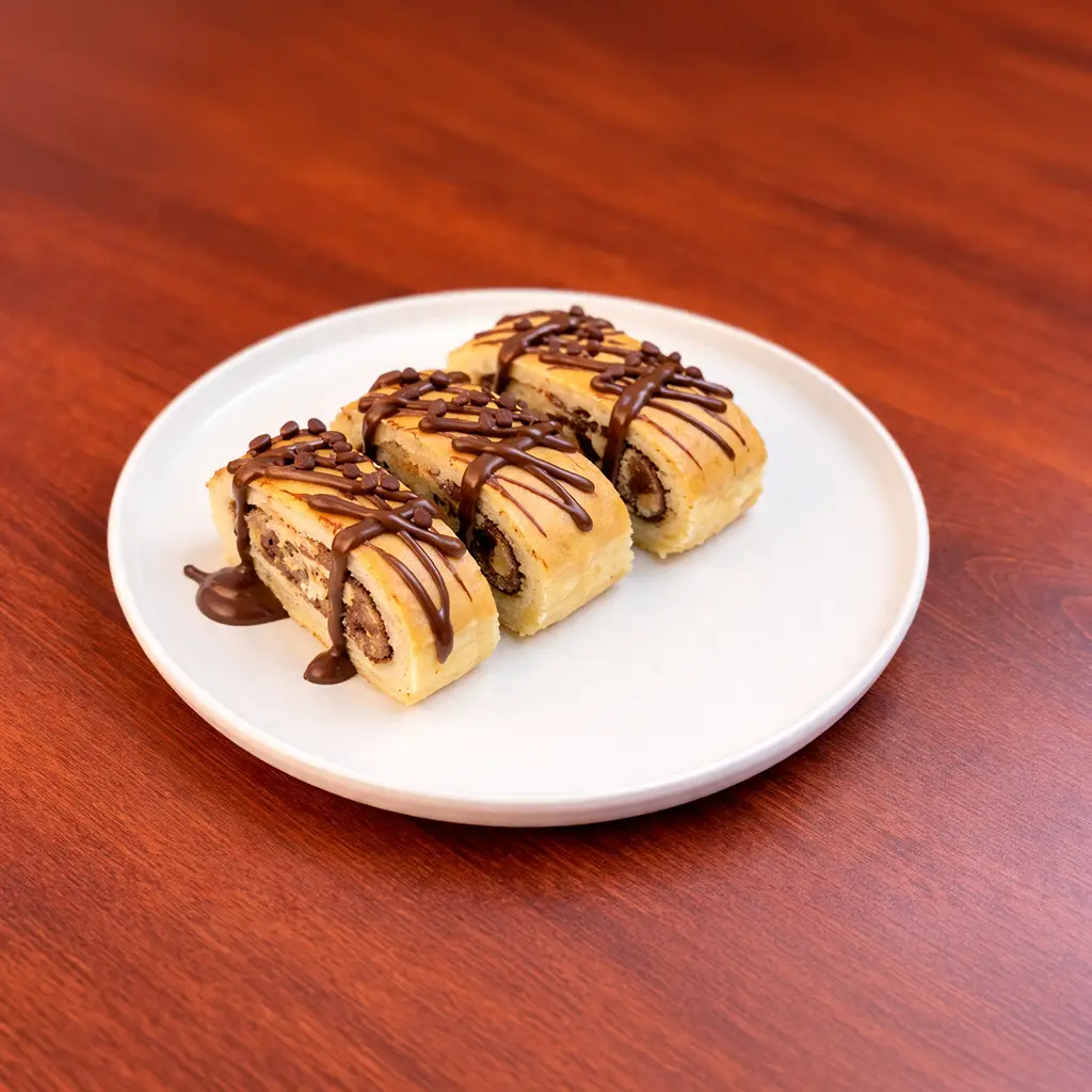 Three sliced chocolate Swiss roll pieces drizzled with chocolate sauce and chocolate chip sprinkles on a white plate at Cafe Galata Guelph