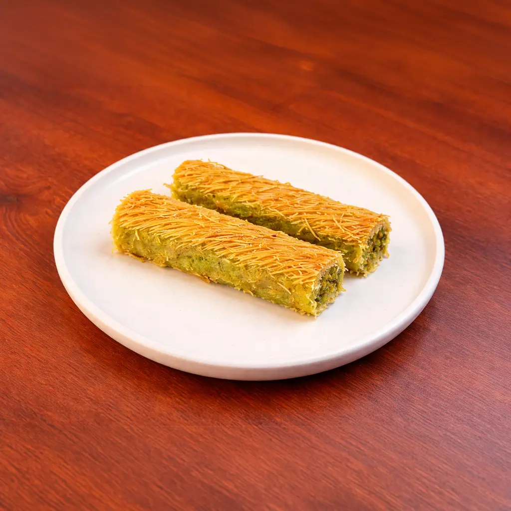 Two pieces of Burma Kadayıf Turkish dessert filled with pistachio and wrapped in golden crispy kataifi pastry served on a white plate at Cafe Galata Guelph